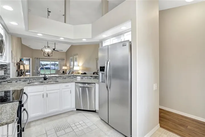 Kitchen with appliances with stainless steel finishes, recessed lighting, light stone countertops, white cabinetry, and a peninsula