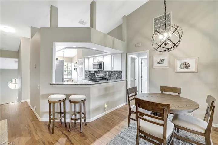 Kitchen with a chandelier, light wood finished floors, appliances with stainless steel finishes, white cabinets, and light stone countertops