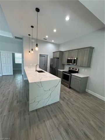 Kitchen with light stone counters, range, wood finish floors, freestanding refrigerator, and decorative light fixtures