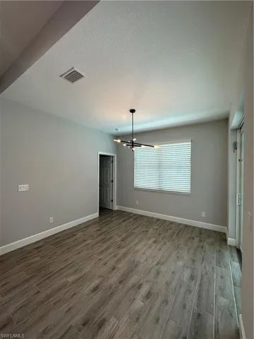 Unfurnished room featuring dark wood finished floors, hanging lights, and a textured ceiling