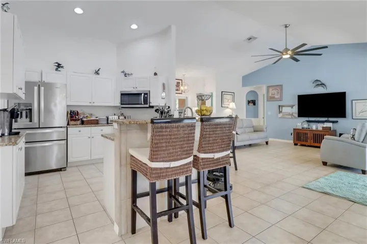 Kitchen featuring stainless steel appliances, high vaulted ceiling, open floor plan, light tile patterned flooring, and ceiling fan
