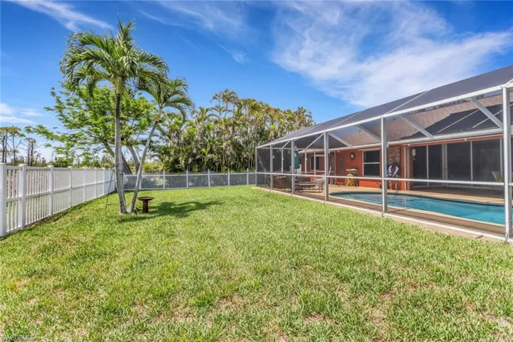 View of fenced-in yard with an outdoor pool, above ground hot tub, and lanai, and remaining grass area