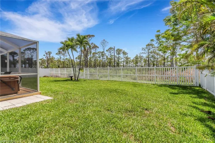 View of fenced-in yard featuring a hot tub, lanai, and grass