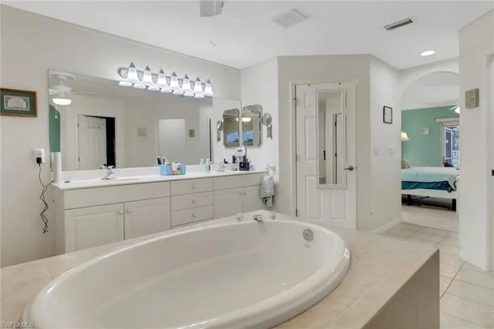 Full bathroom with ceiling fan, double vanity, a stand alone soaking bath, baseboards, and tile patterned floors