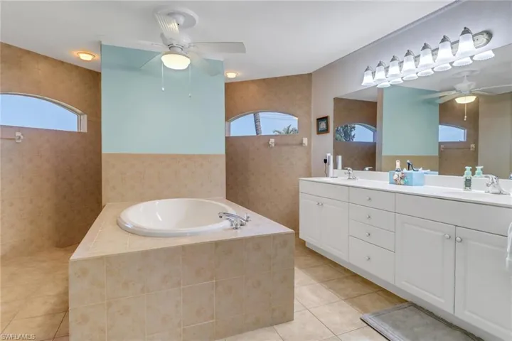 Full bathroom featuring a ceiling fan, tile patterned flooring, a bath, natural light, vanity light, and tile walls