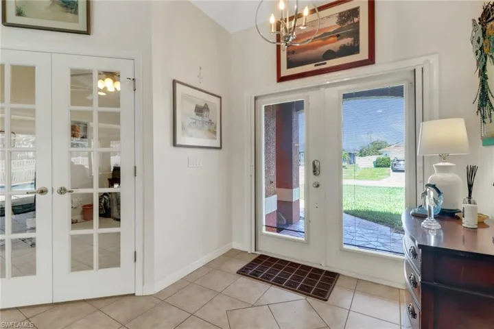 Foyer with french doors, a chandelier, light tile patterned flooring, and baseboards