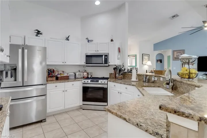Kitchen with stainless steel appliances, a sink, high vaulted ceiling, light tile patterned floors, and ceiling fan
