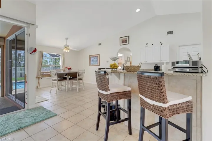 Kitchen with arched walkways, white cabinets, a ceiling fan, light tile patterned floors, and a kitchen bar