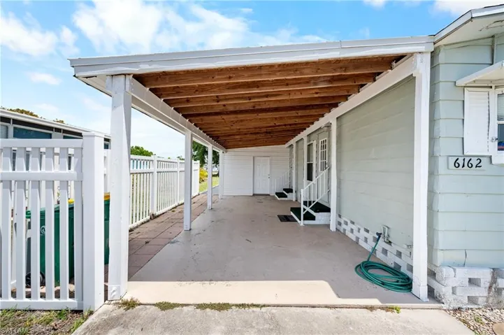 Covered carport with exposed wood ceiling beams, concrete flooring, and white support columns