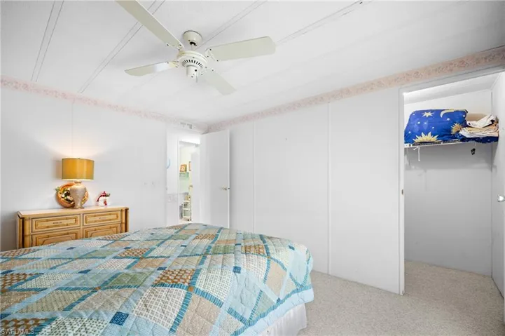Carpeted interior space featuring a ceiling fan, white paneled walls, and a recessed closet with shelving