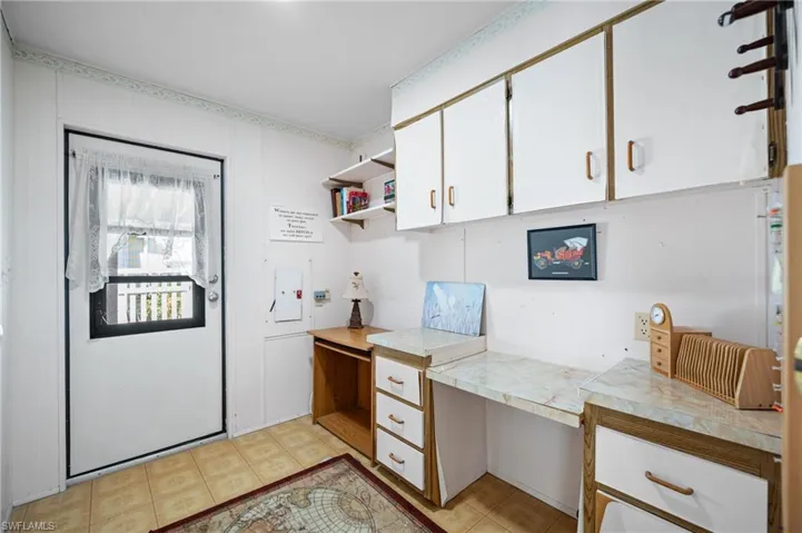 Functional utility space featuring a white exterior door with window, overhead cabinetry, built-in desk with laminate countertop, open shelving, and tiled flooring
