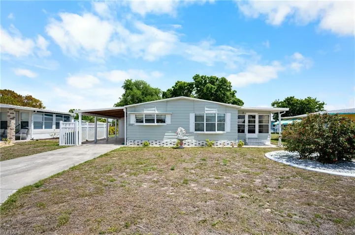 Light blue siding exterior with white window trim and shutters, covered carport, screened porch entry, paved driveway, and established front landscaping with white decorative stones