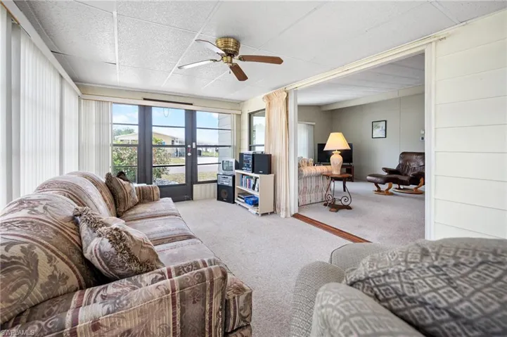Carpeted sunroom featuring a ceiling fan, full-light entry door, and large windows with vertical blinds