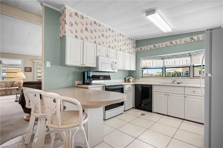 Kitchen featuring white cabinetry, a light-toned countertop with a breakfast bar, white tile flooring, and integrated appliances