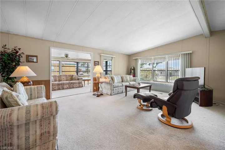 Spacious living area featuring light-toned carpeting and a vaulted ceiling