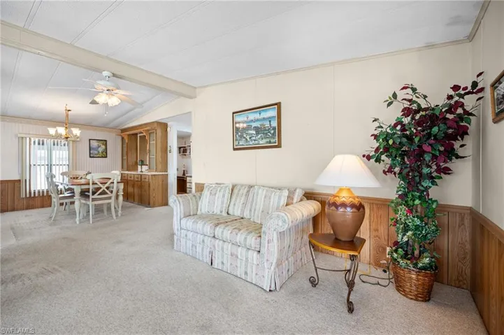 Carpeted living area featuring vaulted ceilings, a dining area with a chandelier, and a built-in wood-finish display cabinet