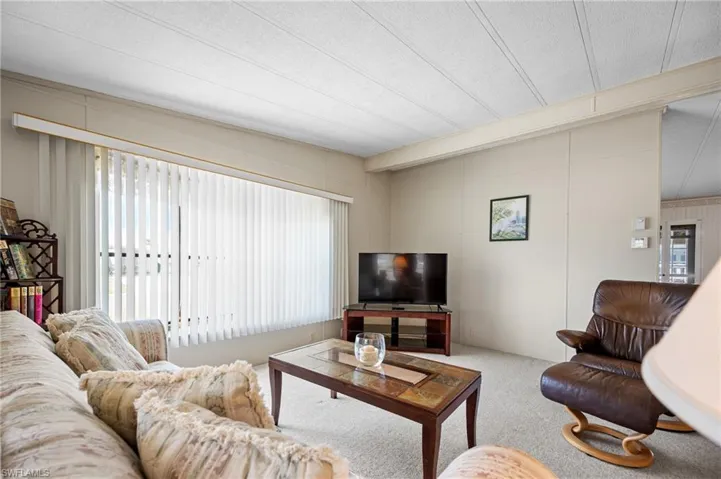 Living area featuring broad window with vertical blinds, textured ceiling, light-toned walls, and carpet flooring