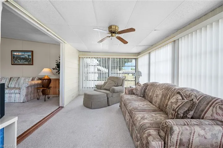 Carpeted sunroom with a ceiling fan, vertical blinds, and a sliding door entry to an additional carpeted room