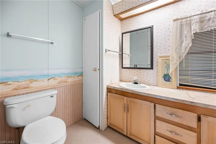 Bathroom featuring a built-in vanity with light wood cabinetry and an integrated sink, a rectangular framed mirror, and panel walls with a beach-themed accent