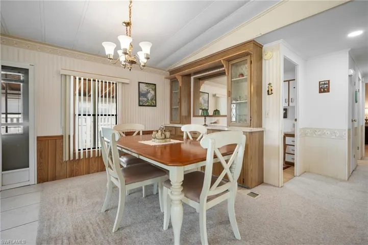 Dining area featuring a built-in hutch with glass-front cabinetry, a brass chandelier, and a large window with vertical blinds