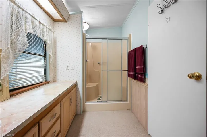 Bathroom featuring a sliding glass shower enclosure, wood-finish cabinetry with a laminate countertop, and a window with blinds