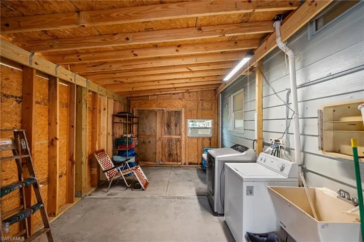 Utility area featuring exposed wood ceiling joists, concrete flooring, a utility sink, and a window