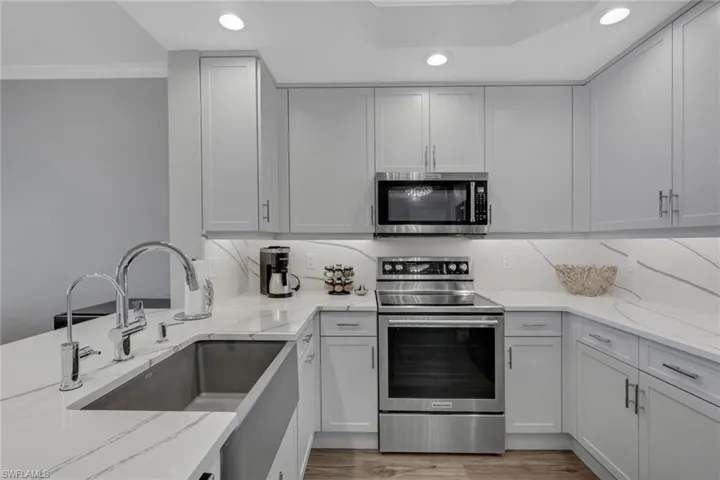 Kitchen with stainless steel appliances, light stone counters, recessed lighting, crown molding, and light wood-style flooring