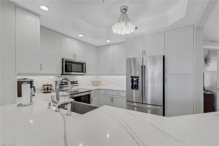 Kitchen featuring stainless steel appliances, ornamental molding, light stone countertops, white cabinetry, and hanging light fixtures