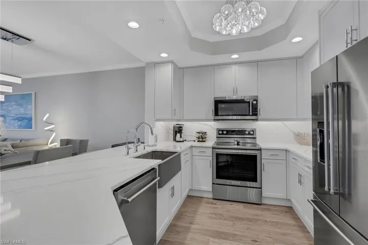 Kitchen featuring ornamental molding, stainless steel appliances, light stone countertops, suspended lighting, and light wood-style flooring