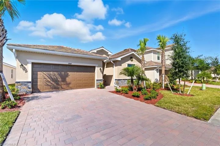View of front facade with stone siding, stucco siding, decorative driveway, a front lawn, and an attached garage