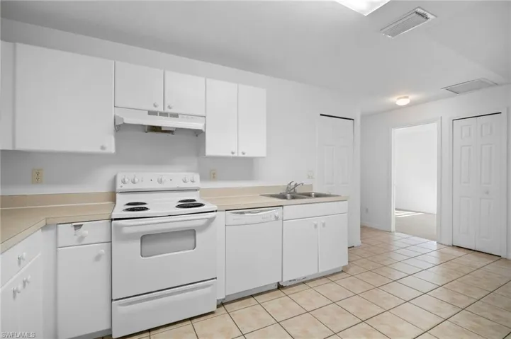 Kitchen featuring white appliances, light countertops, white cabinets, under cabinet range hood, and light tile patterned floors