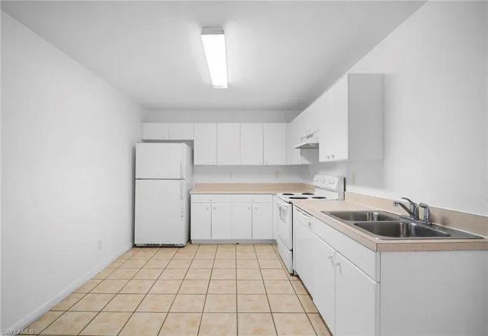 Kitchen featuring white appliances, light countertops, white cabinetry, under cabinet range hood, and light tile patterned floors