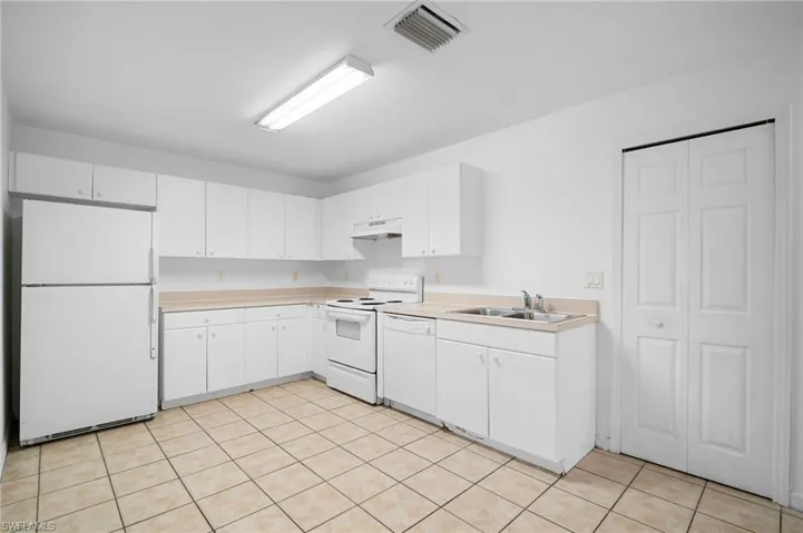 Kitchen with white appliances, light countertops, white cabinetry, under cabinet range hood, and light tile patterned flooring