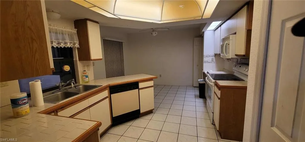 Kitchen with tile countertops, white appliances, light tile patterned flooring, brown cabinetry, and white cabinetry