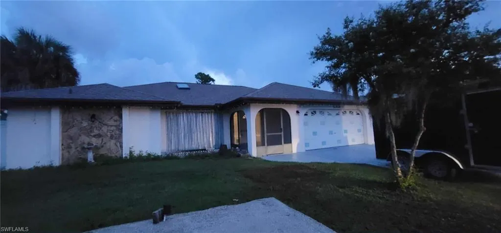 Ranch-style home featuring an attached garage, stone siding, a front lawn, and stucco siding