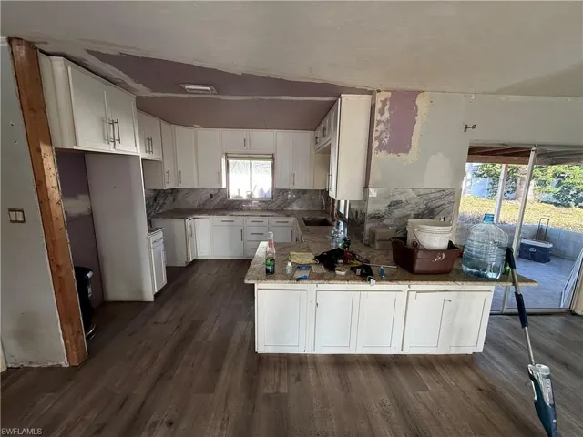 Kitchen with white cabinetry, a peninsula, dark wood-style flooring, light stone counters, and tasteful backsplash