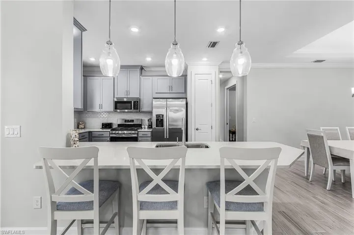 Kitchen featuring a breakfast bar with pendant lighting, light-colored cabinetry, stainless steel appliances, and wood-finish flooring