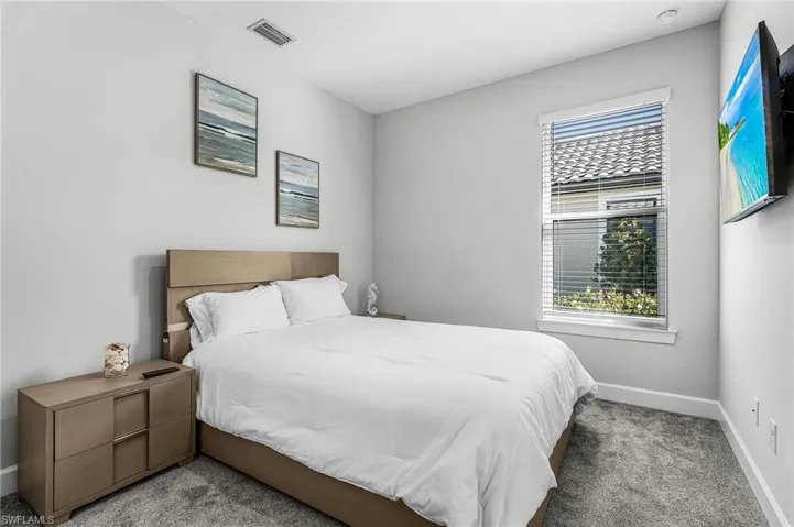 Carpeted bedroom featuring a window with blinds, a wall-mounted flat-screen television, recessed lighting, and a neutral color palette