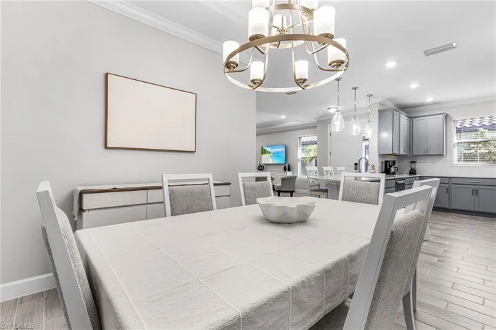 Bright dining area featuring a multi-bulb chandelier, crown molding, and wood-finish flooring