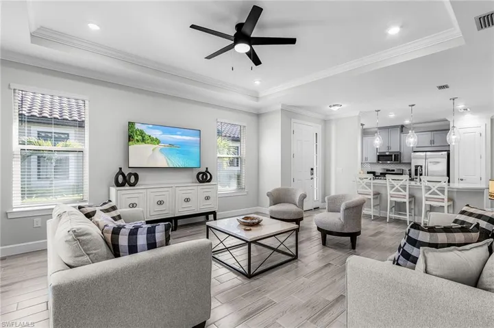 Open-concept living space featuring wood-finish flooring, recessed lighting, and a tray ceiling with a black ceiling fan