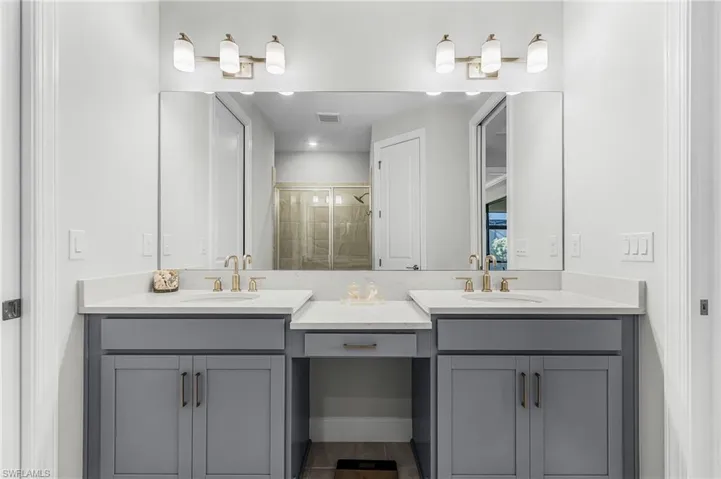 Dual vanity with gray shaker cabinetry, integrated sinks, brushed gold fixtures, and a central vanity area
