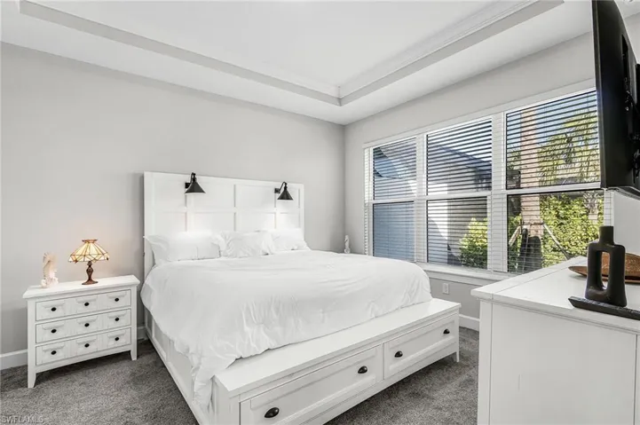 Bedroom featuring a tray ceiling, recessed lighting, and a large window with horizontal blinds