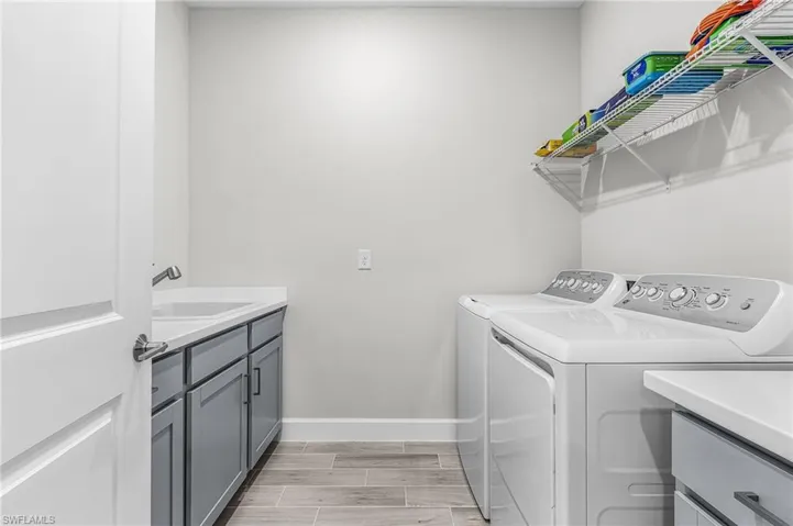 Dedicated laundry room featuring wood-finish tile flooring, a utility sink with a chrome faucet, gray cabinetry with dark hardware, and white countertops