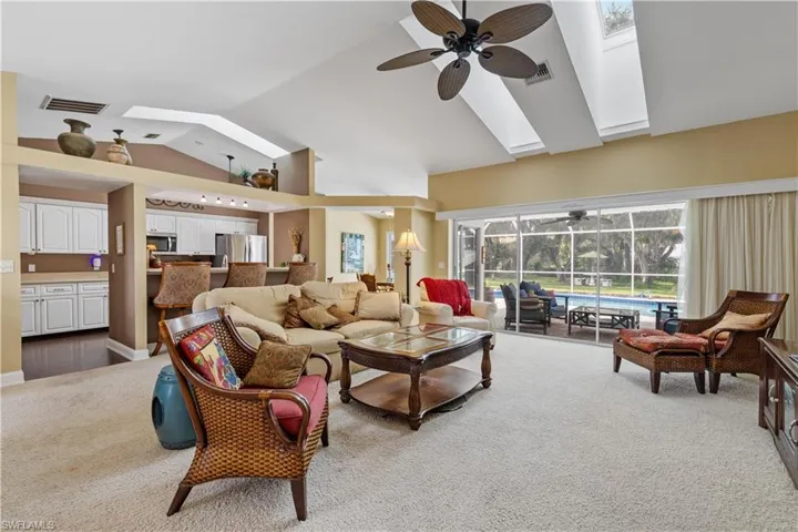 Living room with light colored carpet, lofted ceiling with skylight, and ceiling fan