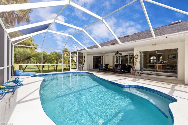 View of pool with glass enclosure, ceiling fan, and a patio
