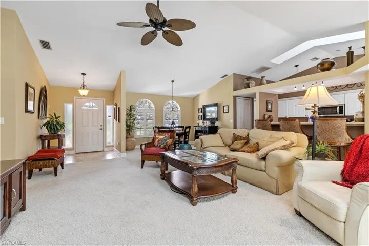 Living room with light carpet, ceiling fan, and lofted ceiling with skylight