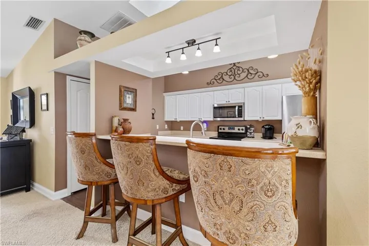 Kitchen featuring stainless steel appliances, a kitchen breakfast bar, kitchen peninsula, a tray ceiling, and white cabinets