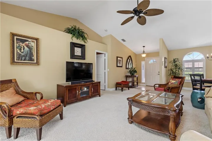 Carpeted living room featuring lofted ceiling and ceiling fan with notable chandelier
