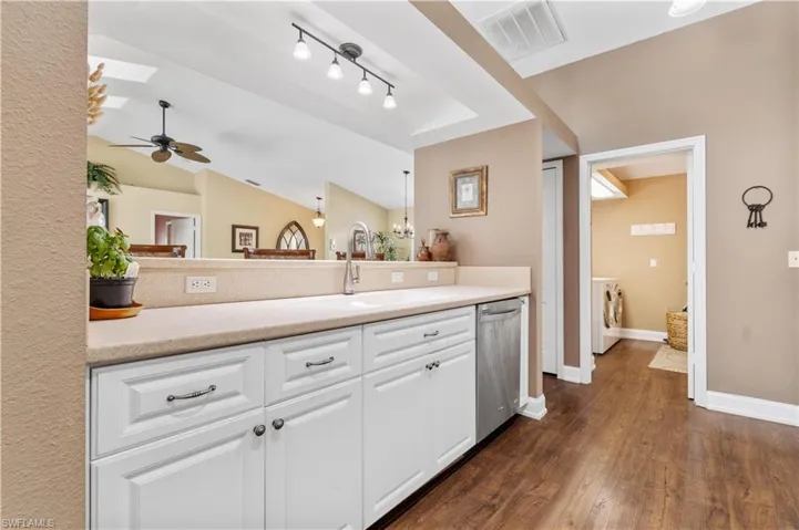 Kitchen featuring dishwasher, lofted ceiling with skylight, sink, dark wood-type flooring, and ceiling fan