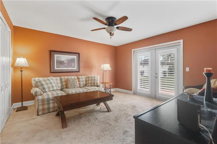 Carpeted living room with ceiling fan and french doors